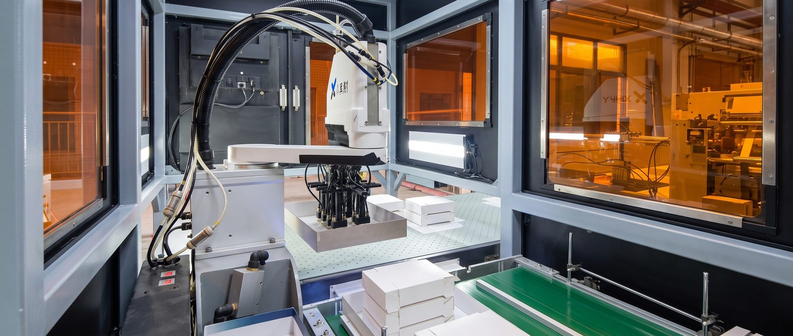Enclosed robotic production cell handling finished boxes